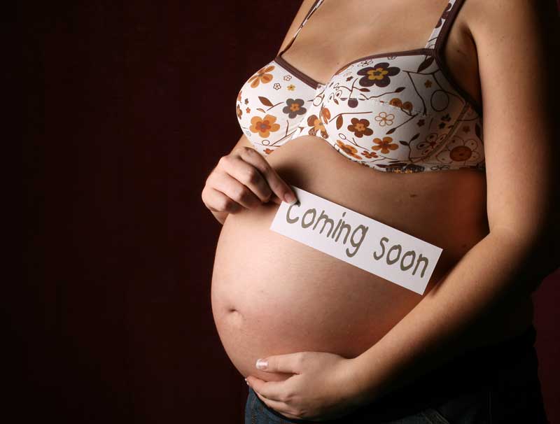 Беременная женщина с табличкой coming soon