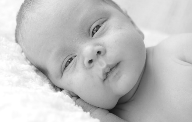 Новорожденный ребенок лежит и щурит глазки